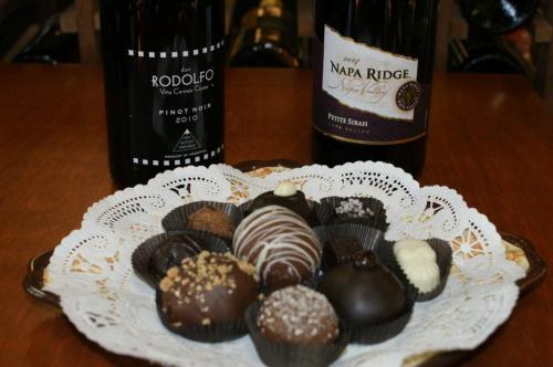 A decorative plate of assorted chocolates with two bottles of wine in the background.