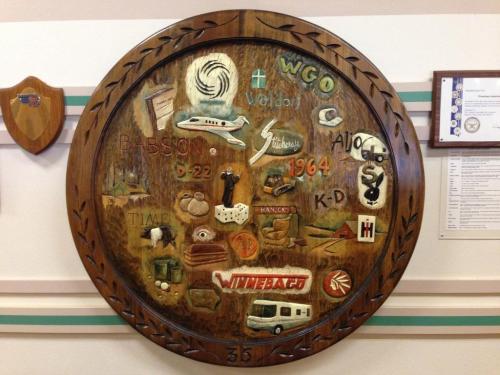 A wooden plaque featuring various carved symbols and text, including a camper, nature scenes, and the year 1964.