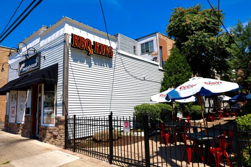 Exterior of BBQ King restaurant with outdoor seating, umbrellas, and a clear blue sky in the background.