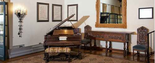 A vintage piano in a stylish room with ornate furniture, a large mirror, and framed artwork on the walls.