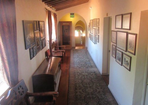 A hallway with framed photos on the walls, wooden benches, and a patterned rug, illuminated by natural light.