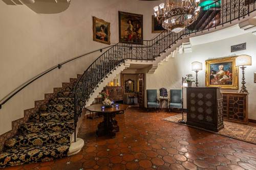 Elegant foyer with a winding staircase, ornate chandelier, and classic artwork, featuring a cozy seating area.
