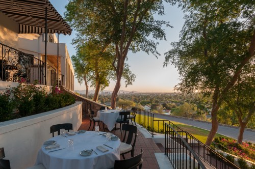 Outdoor dining area with tables set for a meal, surrounded by trees and a scenic view of the landscape.