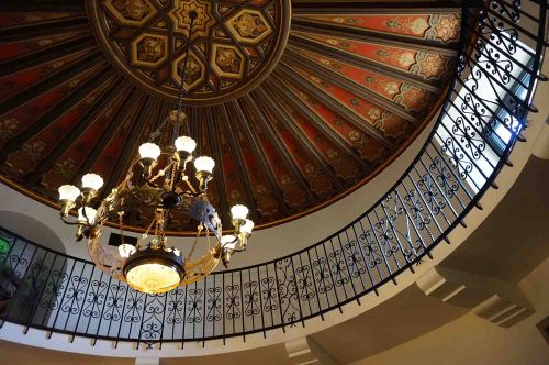 A beautifully designed ceiling with intricate patterns and a chandelier, viewed from below a curved staircase.