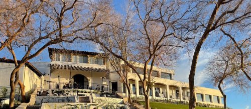 A large, modern building with a terrace, surrounded by bare trees against a blue sky.