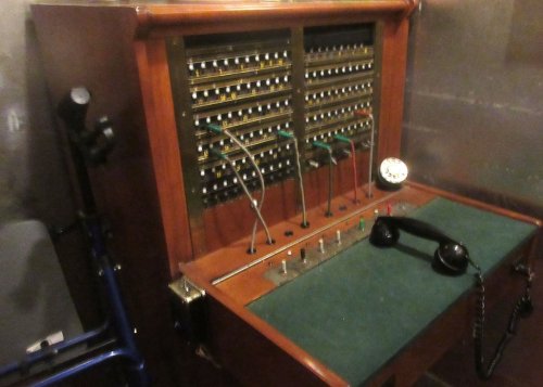 A vintage telephone switchboard with numerous wires, buttons, and a classic handset on a green felt surface.
