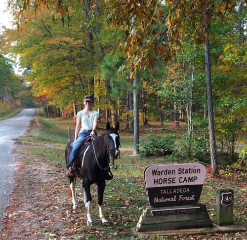 A person on a horse near a sign for Warden Station Horse Camp in Talladega National Forest, surrounded by autumn trees.