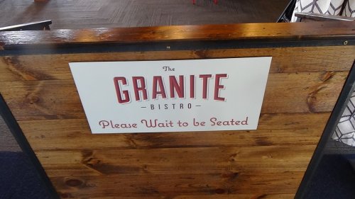 Sign for "The Granite Bistro" with a message: "Please Wait to be Seated." Wooden background.