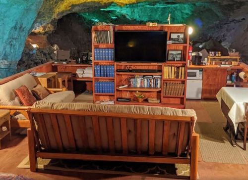 Cozy cave interior with wooden furniture, a large TV, bookshelves, and soft lighting, creating a unique living space.