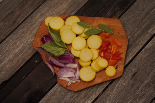 Sliced yellow squash, red bell pepper, and red onion arranged on a wooden cutting board.