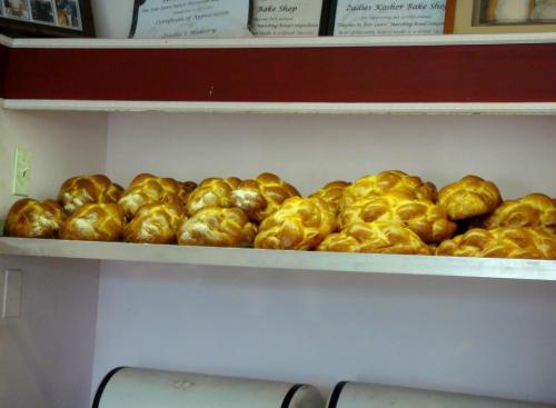 A shelf filled with freshly baked golden challah loaves, showcasing their shiny crusts and braided shapes.