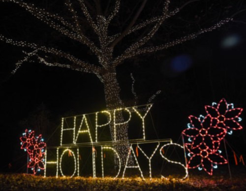 A tree adorned with colorful lights displays a sign that reads "HAPPY HOLIDAYS" in bright letters.
