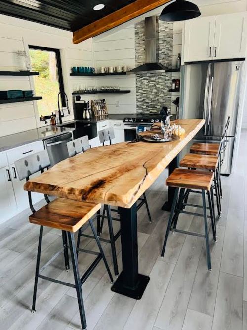 Modern kitchen featuring a large wooden island, metal stools, stainless steel appliances, and a stylish backsplash.