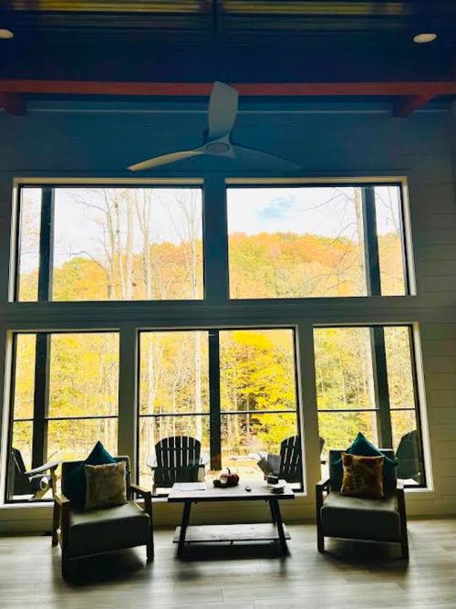 Cozy interior with two chairs and a coffee table, framed by large windows showcasing a colorful autumn landscape outside.