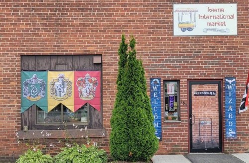 A brick building with a sign for "Keene International Market" and banners featuring Hogwarts house crests.