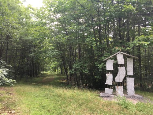A wooded path leads to a unique stone sculpture surrounded by lush greenery.