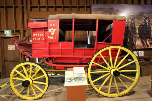 A vintage Wells Fargo mail wagon with red and yellow colors displayed in a museum setting.
