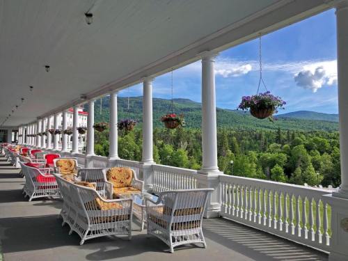 A scenic porch with wicker chairs and hanging flower baskets, overlooking lush green mountains and a blue sky.