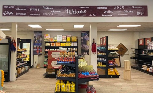 A store interior with shelves of products and a welcome sign in multiple languages on the wall.