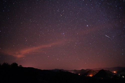 A starry night sky filled with stars and a faint glow from distant mountains and valleys below.