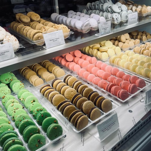A display case filled with colorful macarons in various flavors, arranged in neat rows.