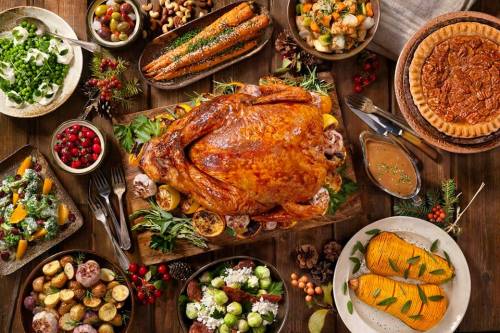 A festive table spread with a golden roasted turkey, sides of vegetables, potatoes, and a pecan pie.
