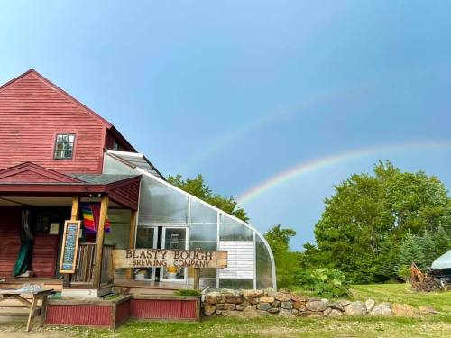 A red building with a sign for Blasty Bough Brewing Company, featuring a greenhouse and a rainbow in the sky.