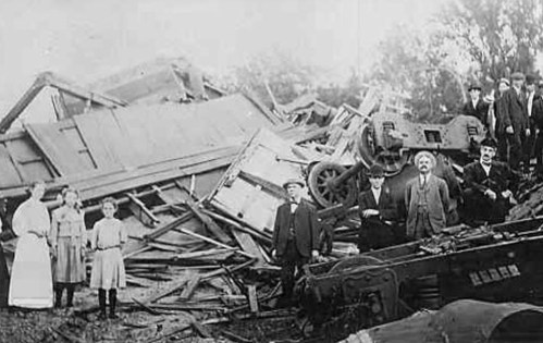 Historical photo of a group of people standing among the ruins of a collapsed building and overturned machinery.