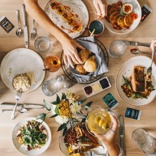 A table filled with various dishes, drinks, and a floral centerpiece, with hands reaching for food.