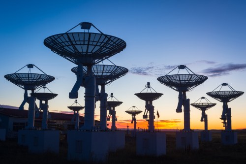 Silhouetted satellite dishes against a colorful sunset sky, creating a striking contrast in the landscape.