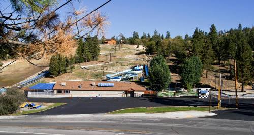 A view of a water park with slides, surrounded by trees and a clear blue sky, near a road.