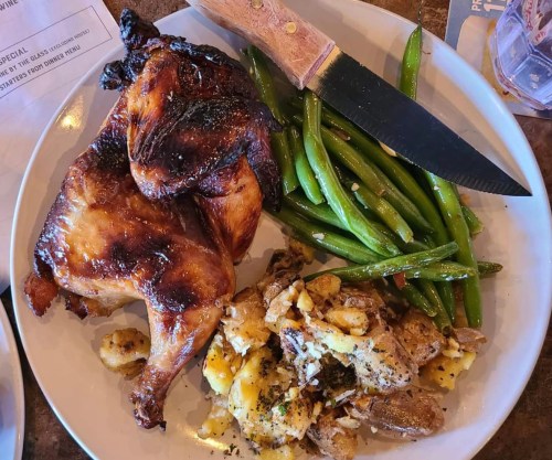 A plate with grilled chicken, green beans, and cheesy potatoes, accompanied by a knife.