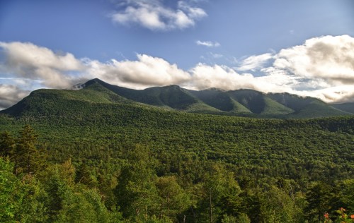 A panoramic view of lush green mountains under a partly cloudy sky, showcasing nature's beauty and tranquility.