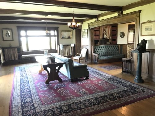 A spacious, vintage living room with a green sofa, wooden furniture, and a large area rug, featuring classic decor.