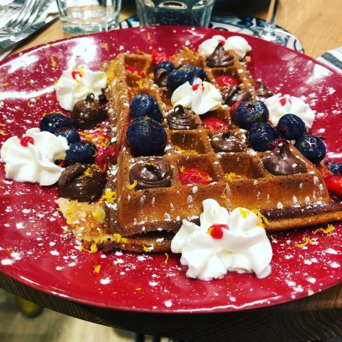 A plate of waffles topped with chocolate, blueberries, whipped cream, and cherries, garnished with orange zest.