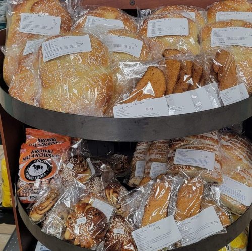A display of various baked goods, including rolls, cookies, and pastries, all packaged and labeled on a metal shelf.