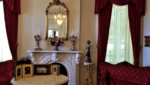 Elegant room featuring a marble fireplace, vintage decor, red drapes, and a round table with framed photos.