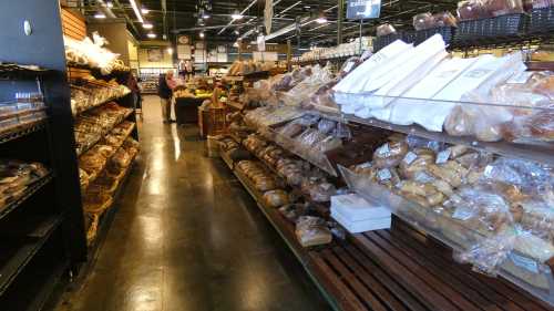 A bakery aisle filled with various types of bread and pastries on display, with customers in the background.