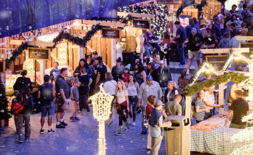A bustling holiday market with crowds, festive stalls, and decorations, creating a lively winter atmosphere.