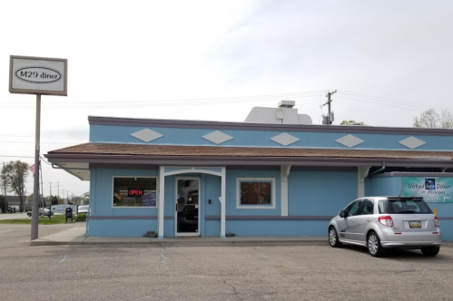 A blue diner building with an "Open" sign and a parked car outside, under a cloudy sky.