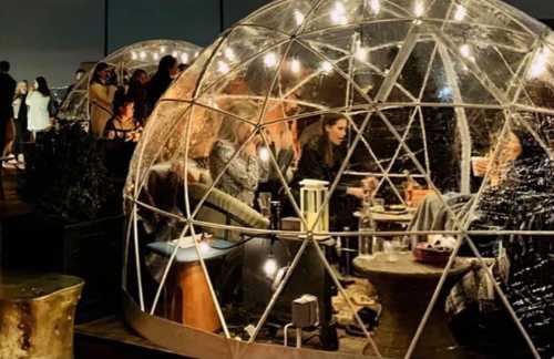 A cozy outdoor setting with transparent domes, people socializing inside, and string lights creating a warm atmosphere.