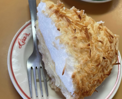 A slice of coconut cream pie topped with toasted coconut, served on a plate with a fork.