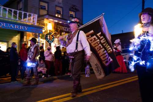 A parade participant holds a banner reading "Living Legends," surrounded by festive lights and onlookers.