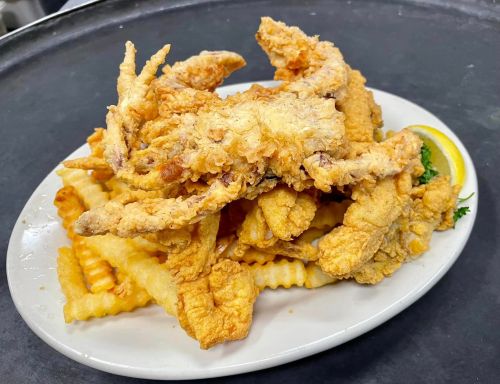A plate of crispy fried soft-shell crabs served on a bed of crinkle-cut fries, garnished with a lemon wedge.