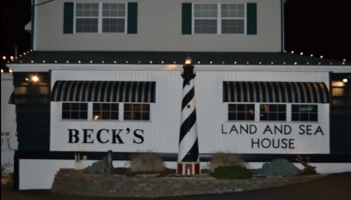 Exterior of Beck's Land and Sea House, featuring a striped lighthouse and decorative lights at night.