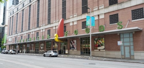 Exterior of a grocery store with large colorful signage, featuring a modern building and parked cars along the street.