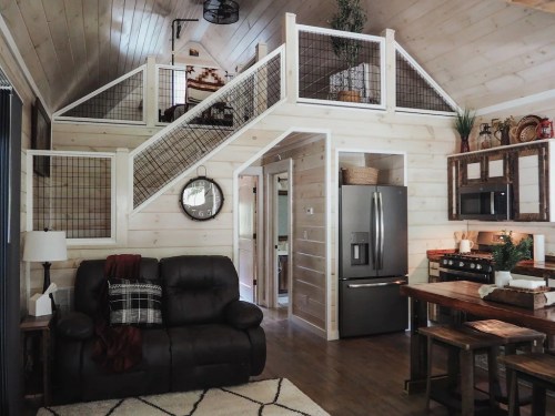 Cozy interior of a modern cabin featuring a living area, kitchen, and a staircase leading to a loft.