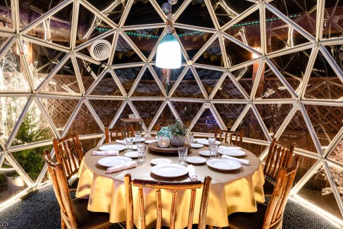 A cozy dining setup inside a geodesic dome, featuring a round table with plates and glasses, illuminated by soft lighting.