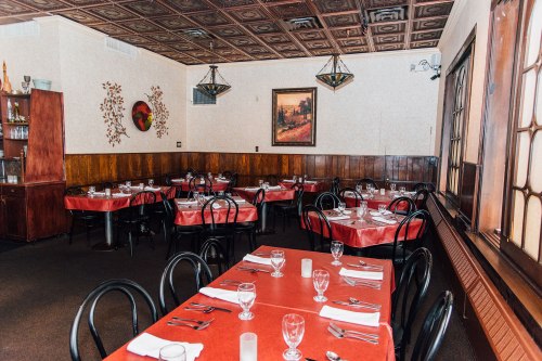 Interior of a restaurant with red tablecloths, black chairs, and wooden paneling, featuring a painting on the wall.