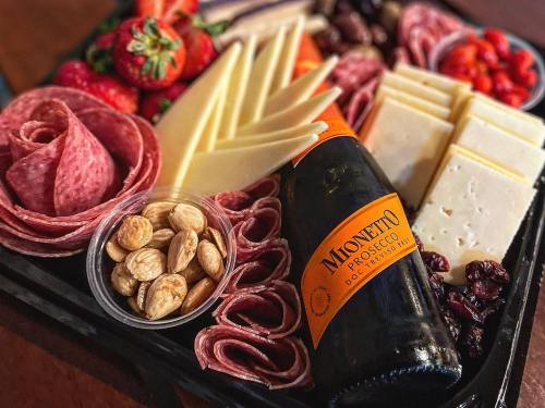 A charcuterie board featuring meats, cheeses, strawberries, nuts, and a bottle of Mionetto Prosecco.